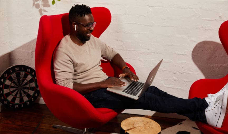 employee sitting in an armchair smiling while using his laptop