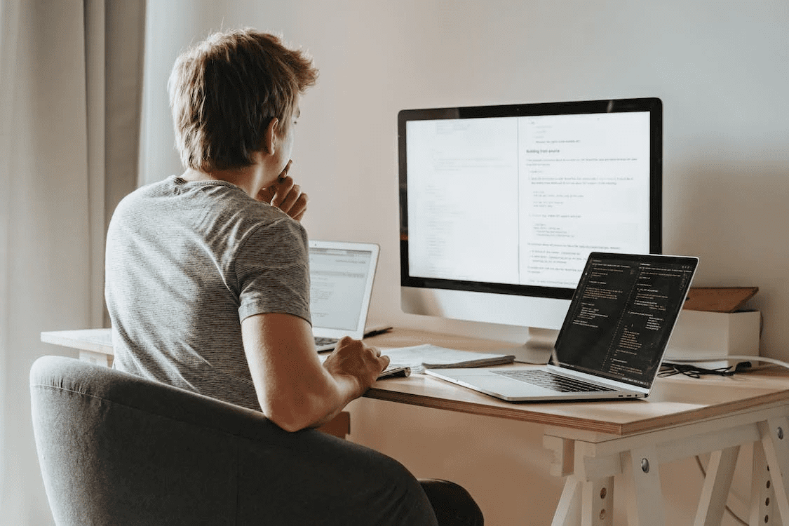 Guy seated at his work from home desk with one monitor and two laptops