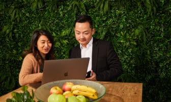 Woman showing man something on a laptop behind a fruit bowl