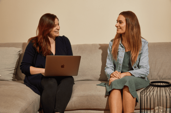 two women sitting on a sofa with an laptop