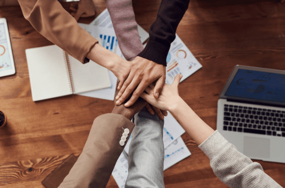 group of diverse employees all putting their hands together in the middle of the table