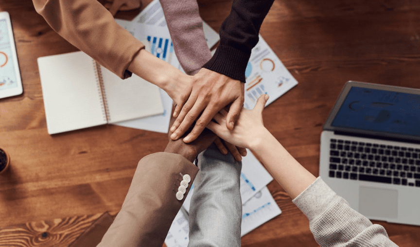group of diverse employees all putting their hands together in the middle of the table